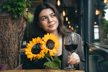 A young woman with a glass of wine and a bouquet of sunflowers in a restaurant.