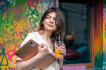A young woman is holding a glass of lemonade and a laptop.