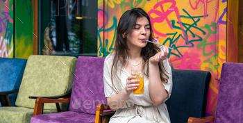 Happy young woman with a glass of lemonade against a bright painted wall.
