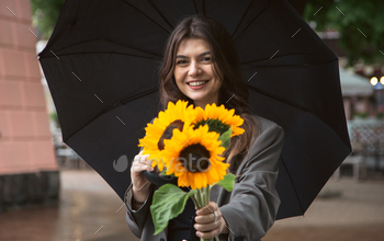 A young woman with a bouquet of sunflowers under an umbrella in rainy weather.