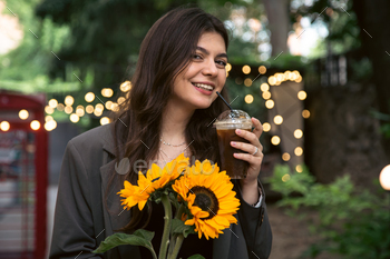 A young woman with a bouquet of sunflowers and a cold coffee drink in the city.