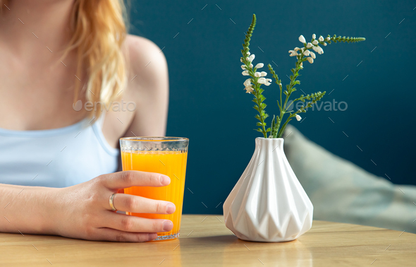 A glass of orange juice on a table in a blue interior. Stock Photo by  puhimec