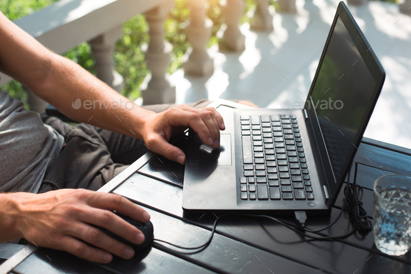 Working at a laptop in the outdoor courtyard - men\'s hands close-up. Home office, remote work
