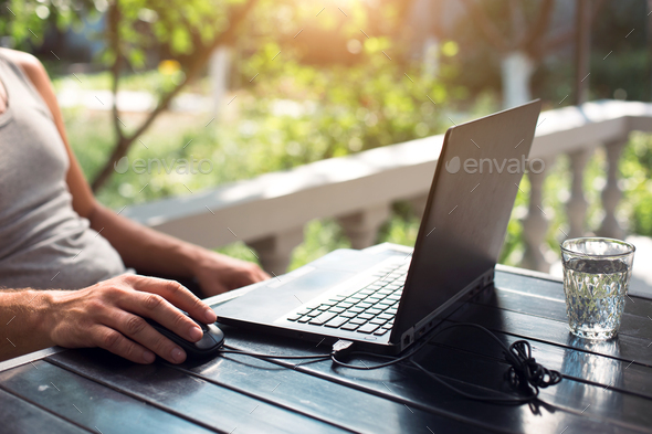 Working at a laptop in the outdoor courtyard - men\'s hands close-up. Home office, remote work