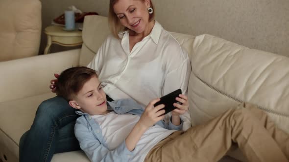 Teenager Lies on the Lap of an Adult Woman and Looks at the Phone