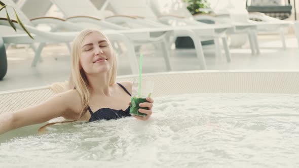 Pleasant Young Woman Relaxing in Jacuzzi with Soft Drink in Her Hand alt