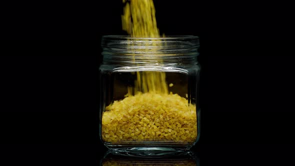 Closeup of Falling Down Bulgur Into Glass Jar on Black Background alt