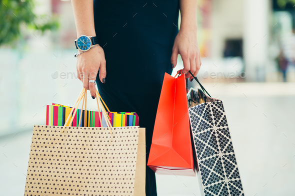 Close-up hands of a young woman holding shopping bags, colored paper bags