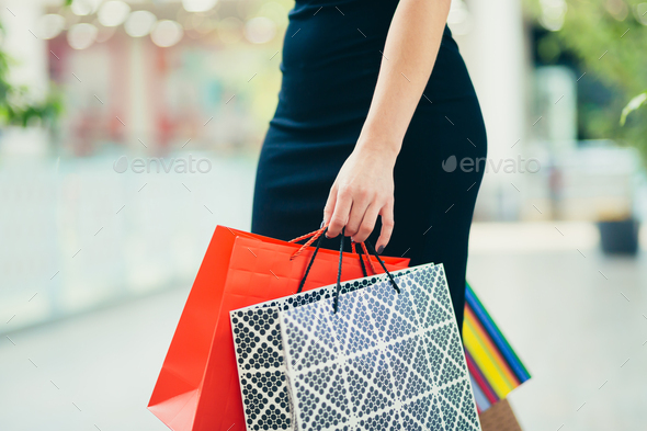 Close-up hands of a young woman holding shopping bags, colored paper bags