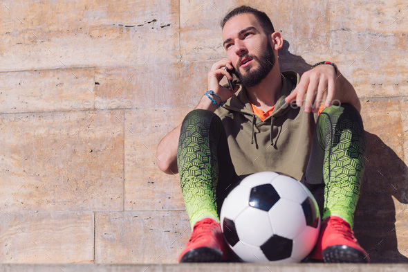 sportsman talking by phone resting with his ball