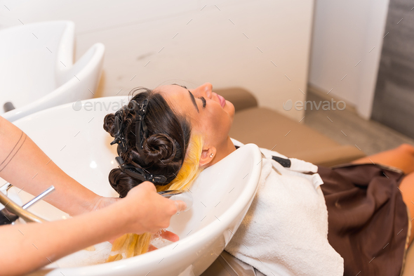 Hairdresser applying a blonde dye to a female client, cleaning her hair