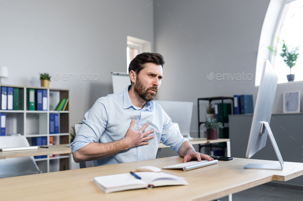A tired young man working at a computer and sitting at a desk in the office - Stock Photo - Images