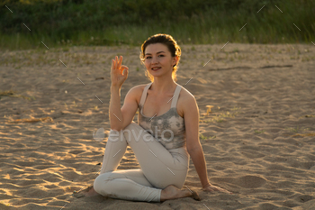 Fit sportive woman practicing yoga on beach in twist pose during sunset