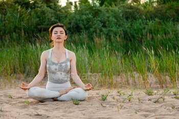 Woman practicing yoga outside in lotus pose on sand