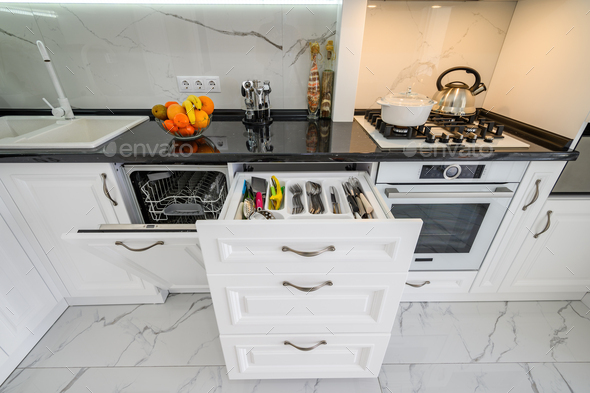 Luxurious white modern kitchen interior, drawers pulled out, dishwasher\'s door open