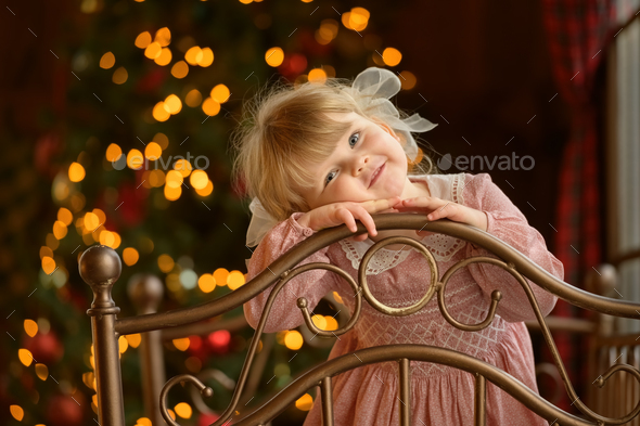 Little cute blond girl standing at headboard of iron bed