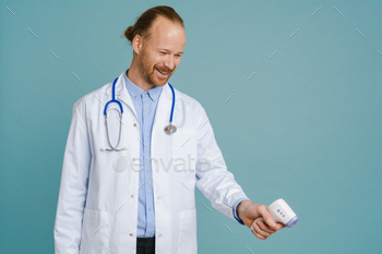 White male doctor wearing lab coat smiling and using thermometer