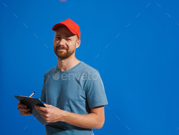 White ginger man wearing cap smiling and writing on clipboard