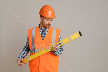 White man worker wearing helmet and vest posing with spirit level tool