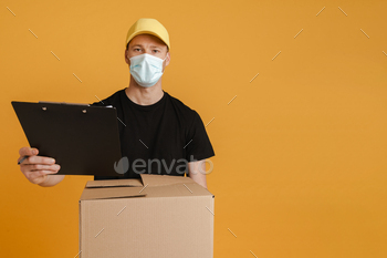White delivery man in face mask posing with cardboard box and clipboard