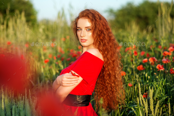 Beautiful girl with very long red hair. Poppy field. Red dress. Concept of health, nature, cosmetics