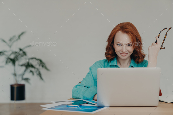 Happy beautiful female financial analyst prepares economic research, works on laptop