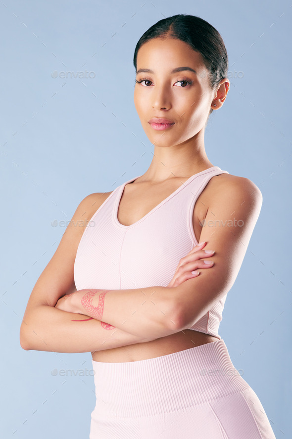 Mixed race fitness woman standing with her arms crossed in studio against a  blue background. Beauti