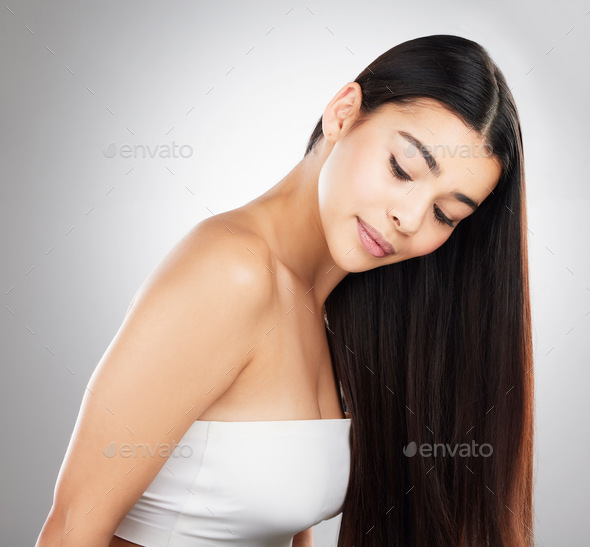 Studio shot of a beautiful young woman showing off her long silky hair against a grey background