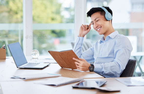 Shot of a young businessman writing in a notebook while listening to music at work