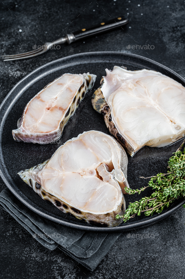 Fresh Raw wolffish o wolf fish Steak on a plate. Black background. Top view