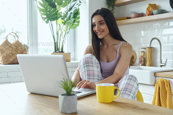 Beautiful woman using laptop while sitting at the kitchen counter at home