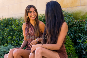 Two friends smiling sitting on a bench in the city enjoying summer, lifestyle