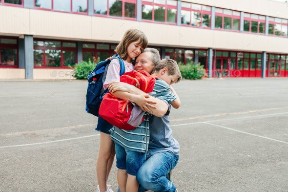 Happy young dad hugging his schoolboy son in front of the school building