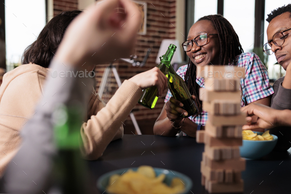 Multicultural happy friends enjoying drinking alcoholic beverage together while playing society
