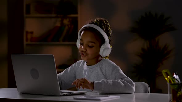 A Girl in White Headphones Listens to Music Singing Along with It Plays Online Games on Her Laptop alt
