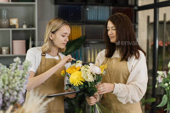 Team of two female florists in beige aprons using tablet