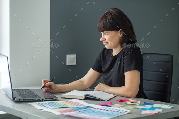 Successful woman plans work schedule, writes in notebook, sitting at workplace with laptop