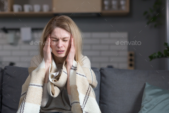 The sick woman is sitting on the couch at home, has a cough and fever, cold and runny nose