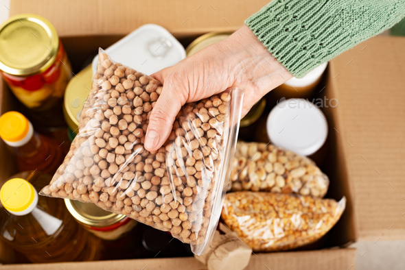 Plastic container with chickpeas in female hand on emergency food box background