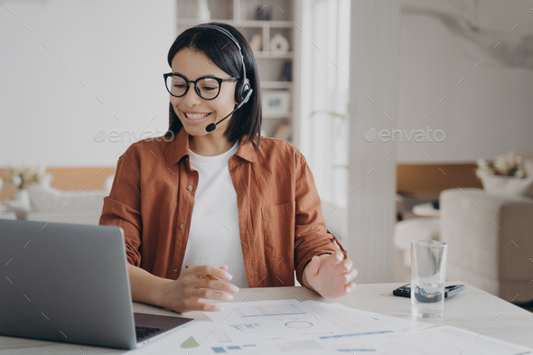 Female coach in glasses, headset conducts online lesson on laptop. E ...