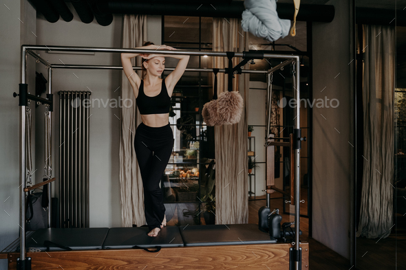 Young slim caucasian female resting on bar of pilates cadillac reformer  Stock Photo by StudioVK