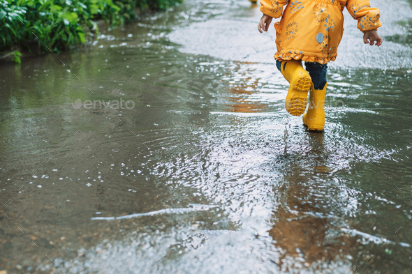 Girl in yellow jacket and rubber boots runs through the puddles