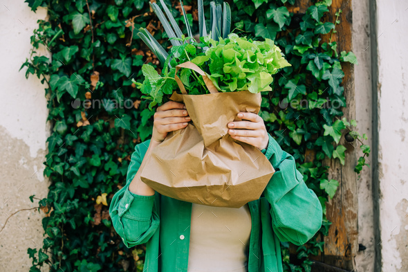 Woman hold bag with vegetables in fornt of a head on wall with ivy background