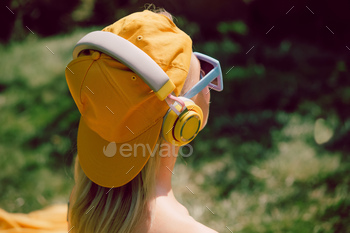 Stylish woman in headphones and yellow cap in outdoor