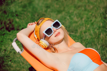 Stylish woman in cap and sunglasses lying on chaise in summer time garden