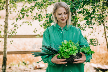 Stylish woman in green shirt hold vegetables in basket on wooden table in outdoor