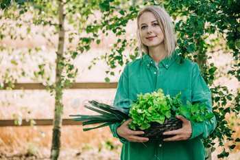 Stylish woman in green shirt hold vegetables in basket on wooden table in outdoor