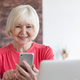 Smiling old elderly senior woman holding smartphone and using laptop at home office. - PhotoDune Item for Sale