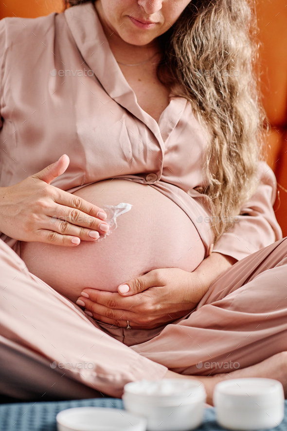 Young pregnant woman applying nutritive night cream on her belly