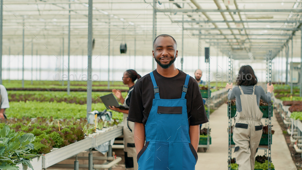 Portrait of smiling african american man posing with arms in pockets while workers push crates with